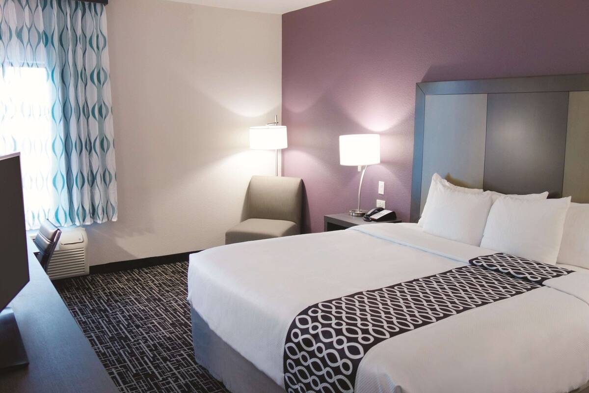 Ett hotellrum med en säng, en stol, ett skrivbord och en lampa.
