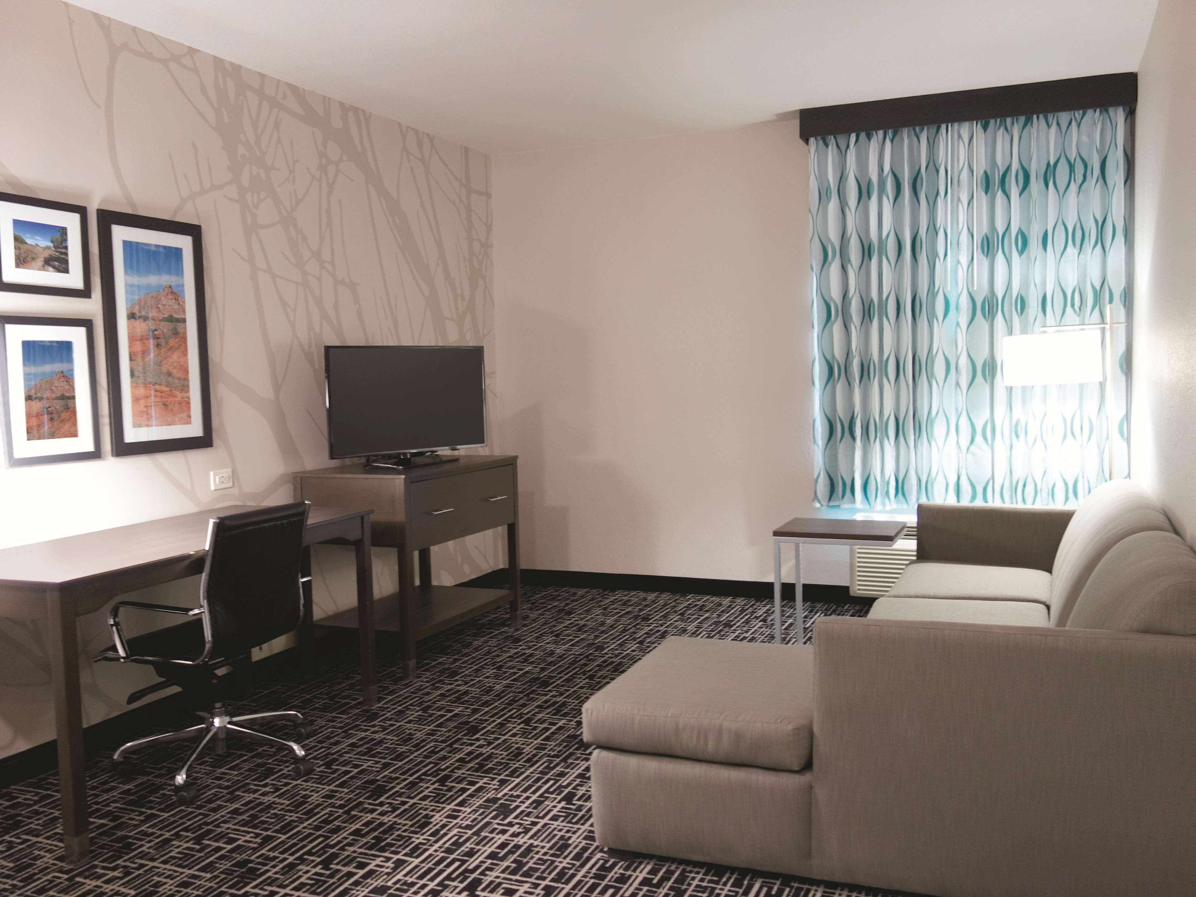 A hotel room with a desk, a television, a sofa, and a patterned carpet.