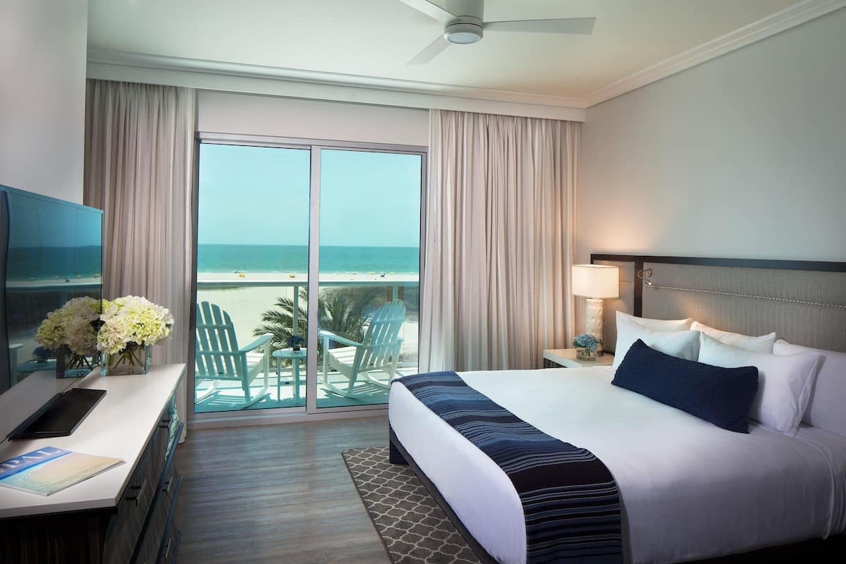 Habitación de hotel con una cama grande, un escritorio con ordenador, televisión y vistas a la playa.