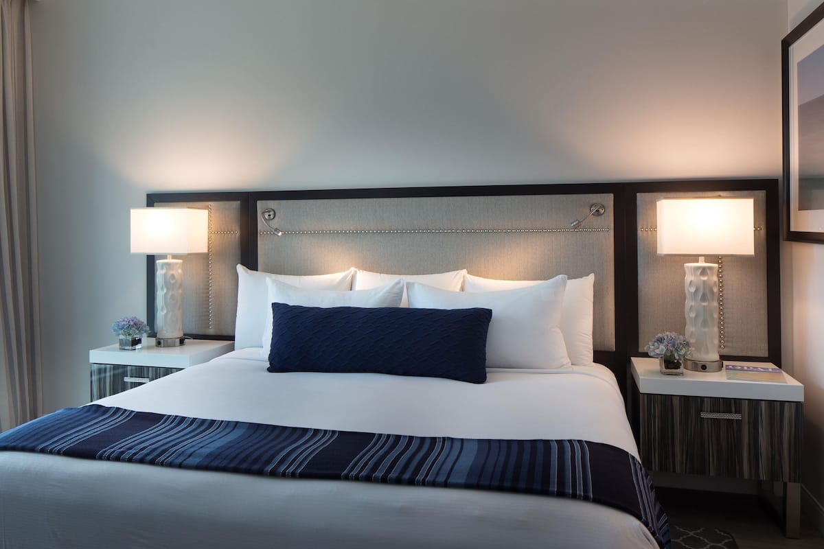 Una habitación de hotel con una cama grande, dos mesitas de noche y lámparas.