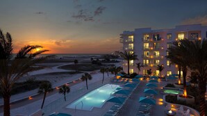 Et resort med swimmingpool, liggestole og udsigt til stranden i solnedgangen.