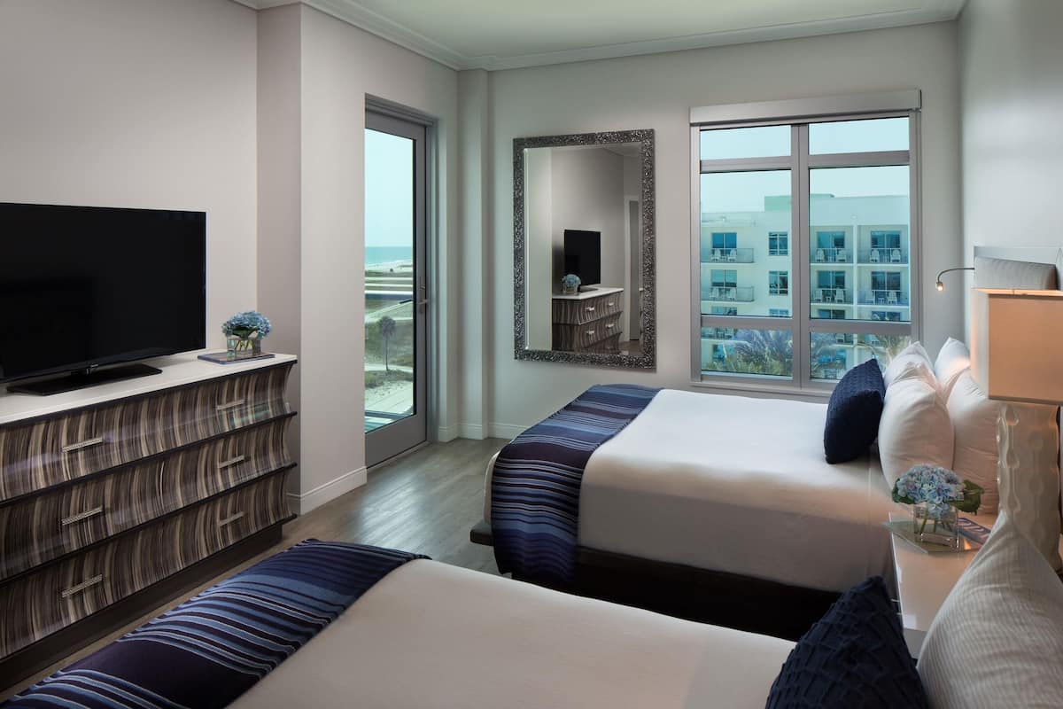 Habitación de hotel con dos camas, televisión, cómoda y un amplio ventanal con vistas a la ciudad.
