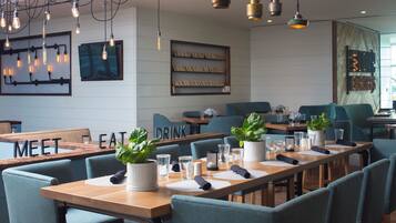 Un restaurante con mesas de madera, sillas color turquesa y lámparas colgantes.