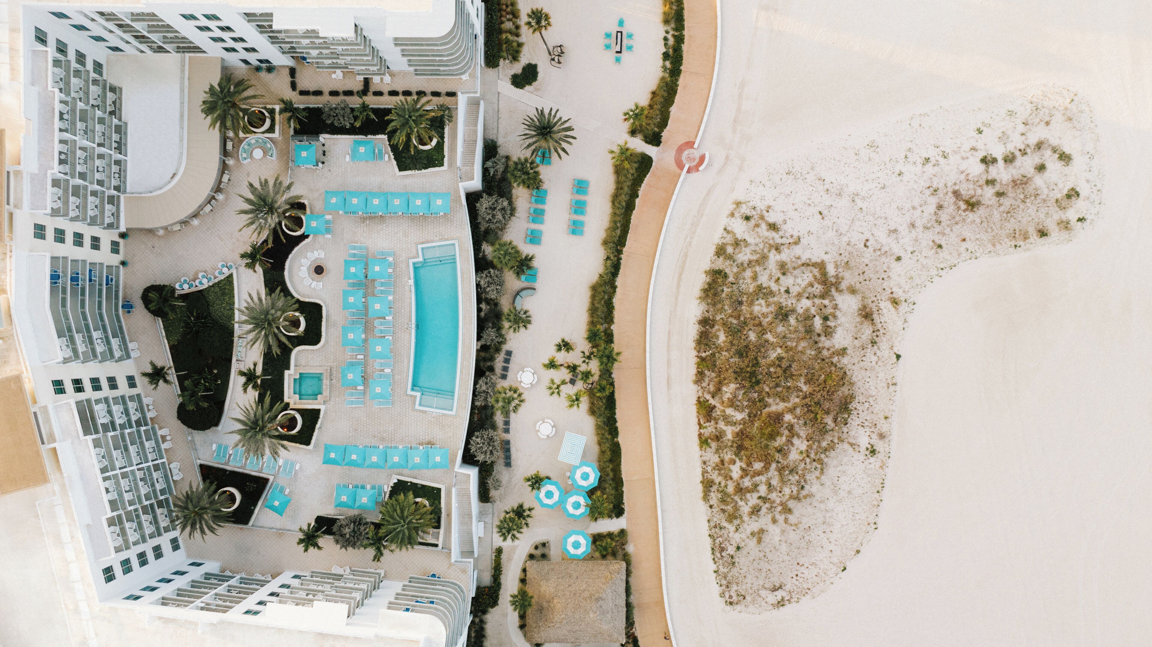 An aerial view of a resort with a swimming pool, sun loungers, and a beach area.