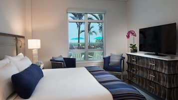 Een hotelkamer met een groot bed, een televisie, een dressoir en een raam met uitzicht op palmbomen.