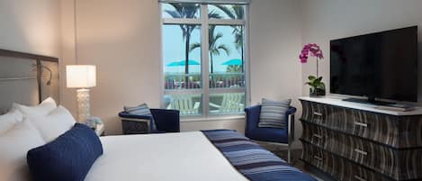 A hotel room with a large bed, a TV, a dresser, and a window with a view of palm trees.