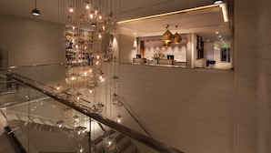 En moderne hotellobby med en glaskonstruktion i trappeform, en reception og et dekorativt lysarmatur.