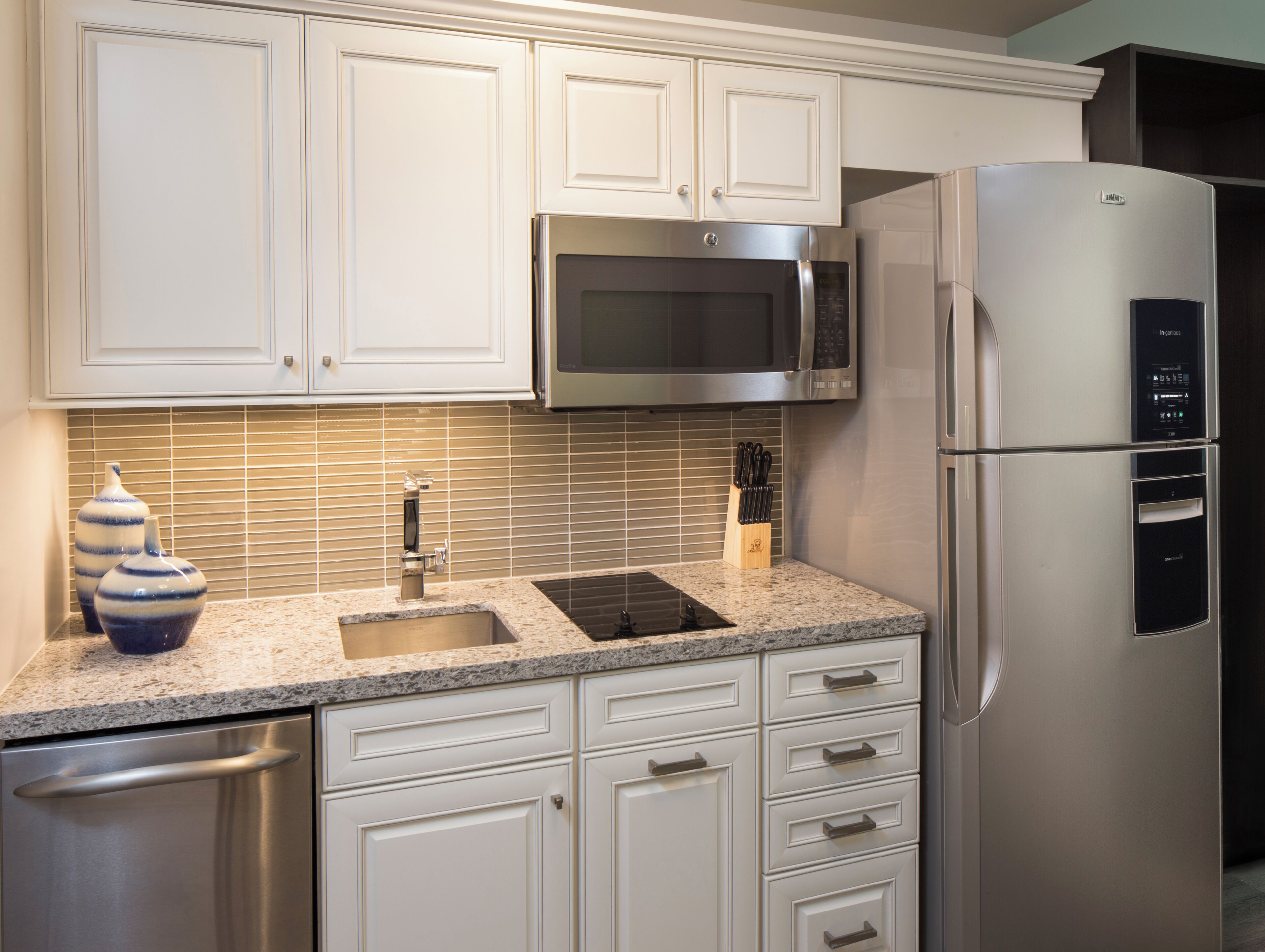 A kitchen with white cabinetry, a stainless steel refrigerator, a microwave, and a sink with a granite countertop.
