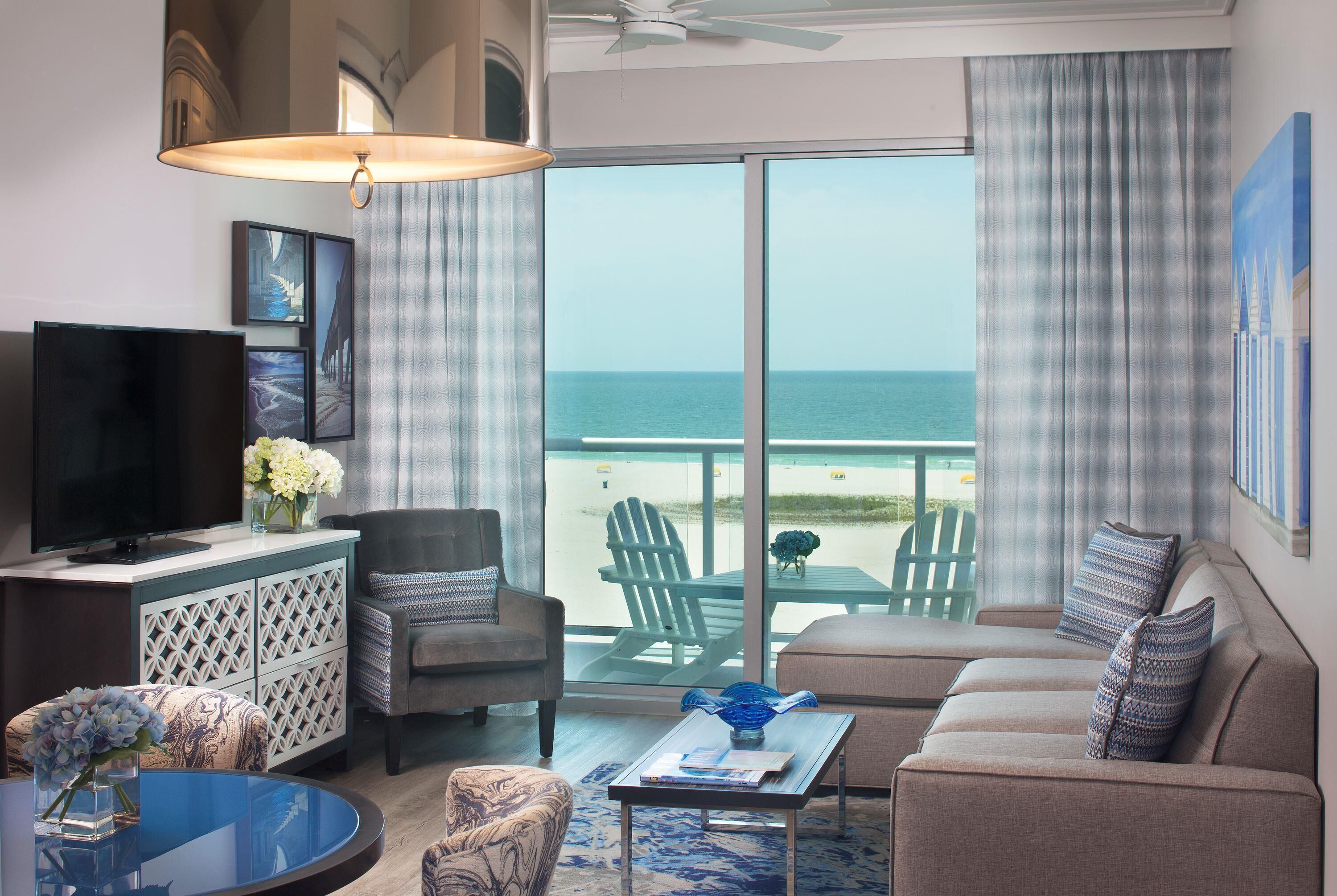 Une chambre d’hôtel dotée d’une grande télévision, d’un canapé, d’une table basse et offrant une vue sur la plage.