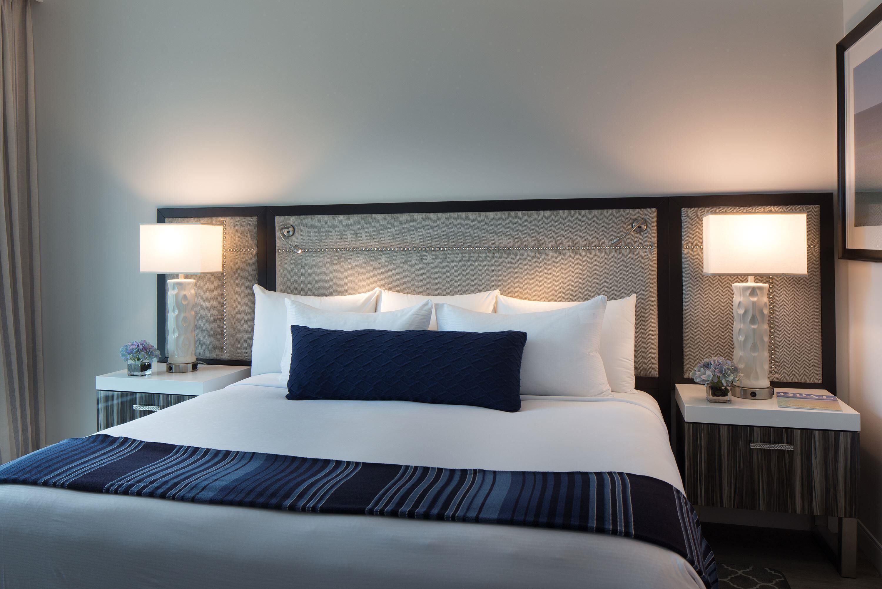 Ett hotellrum med en stor säng, två sängbord och en sänggavel med ett mönstrat utseende.