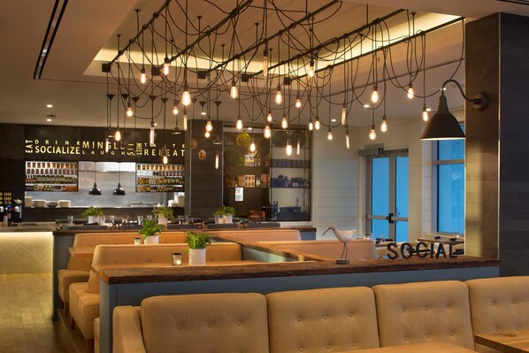Een moderne bar met zitplaatsen, hangende lampen en een zichtbare bar.