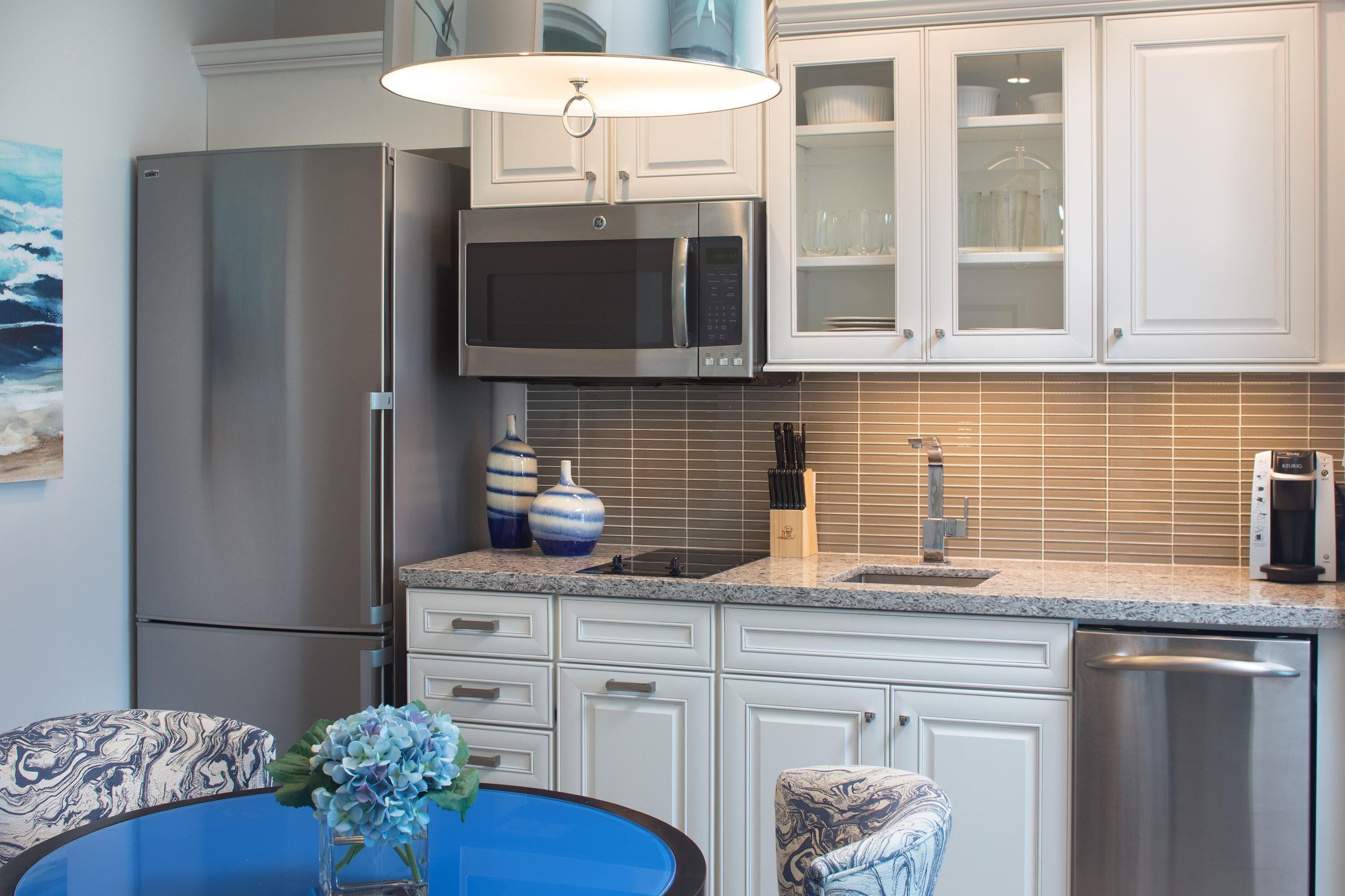 A modern kitchen with stainless steel appliances, white cabinetry, and a blue table with a vase of flowers.