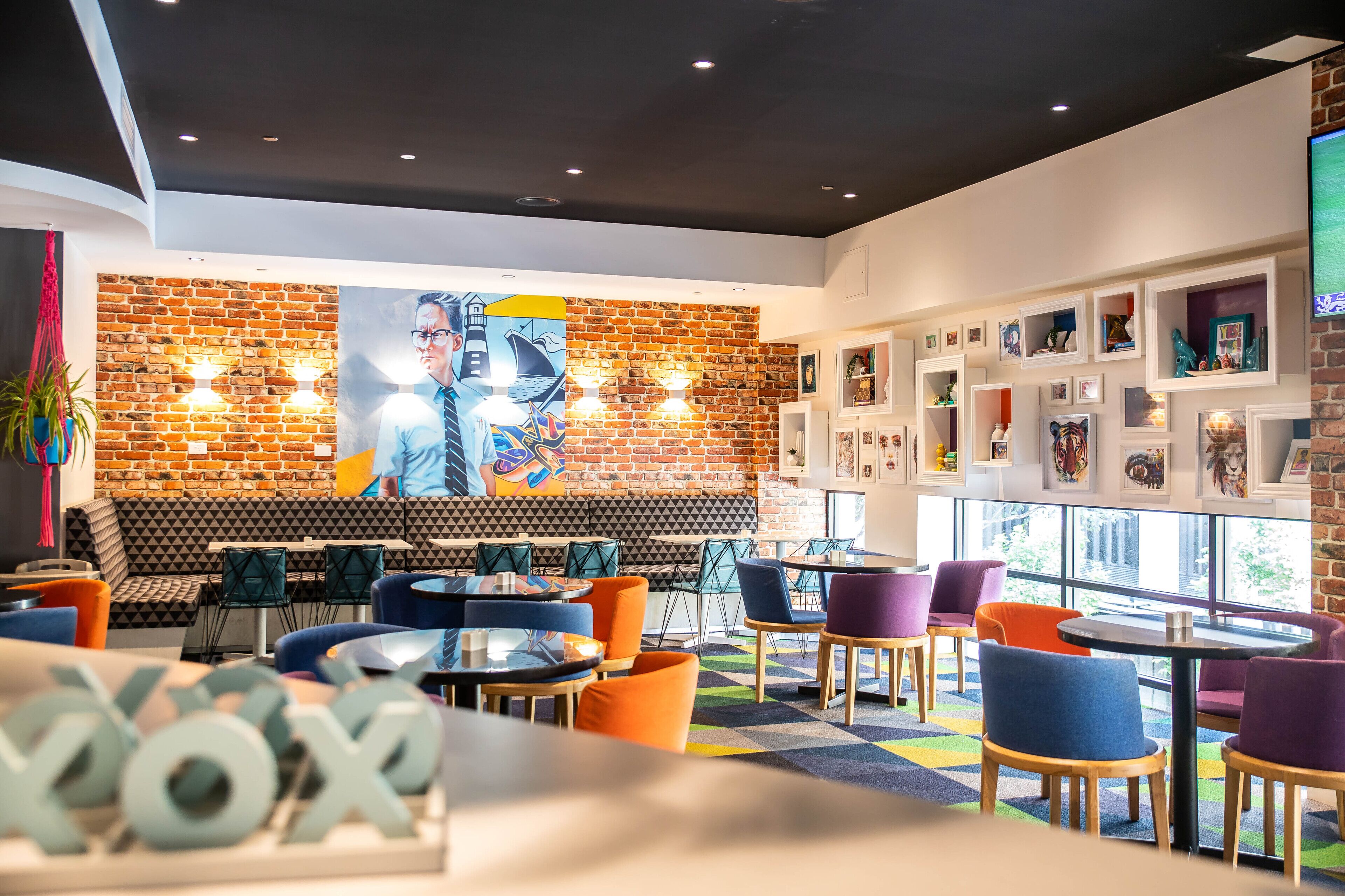 A modern cafe with a brick wall, colorful chairs, and a large mural.