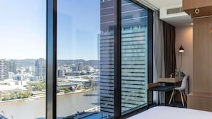 Habitación de hotel con un ventanal grande que ofrece vistas a la ciudad, un escritorio con una silla y una cama.