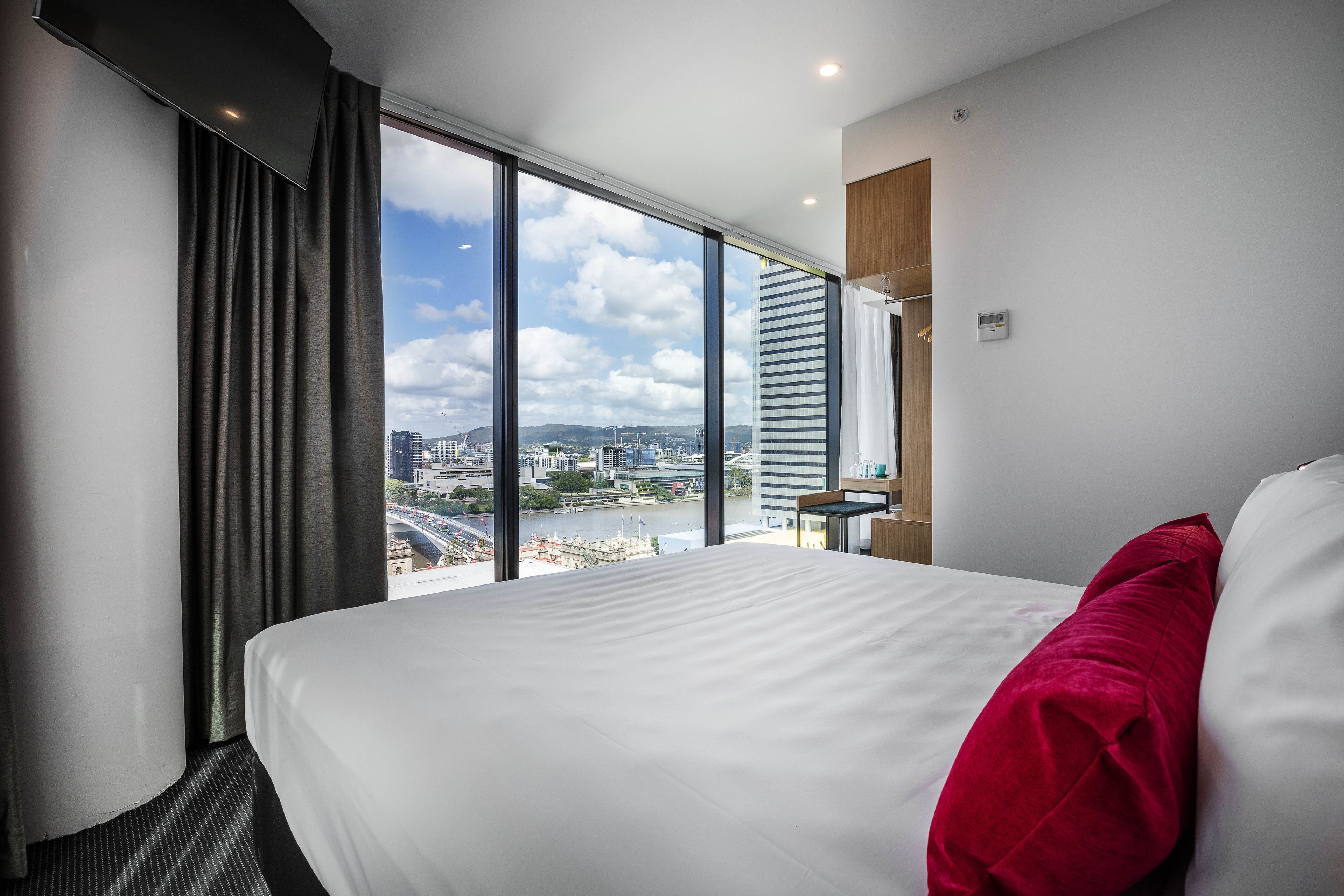 Ein Hotelzimmer mit einem großen Bett, Blick auf eine Stadtlandschaft durch raumhohe Fenster und modernem Design.