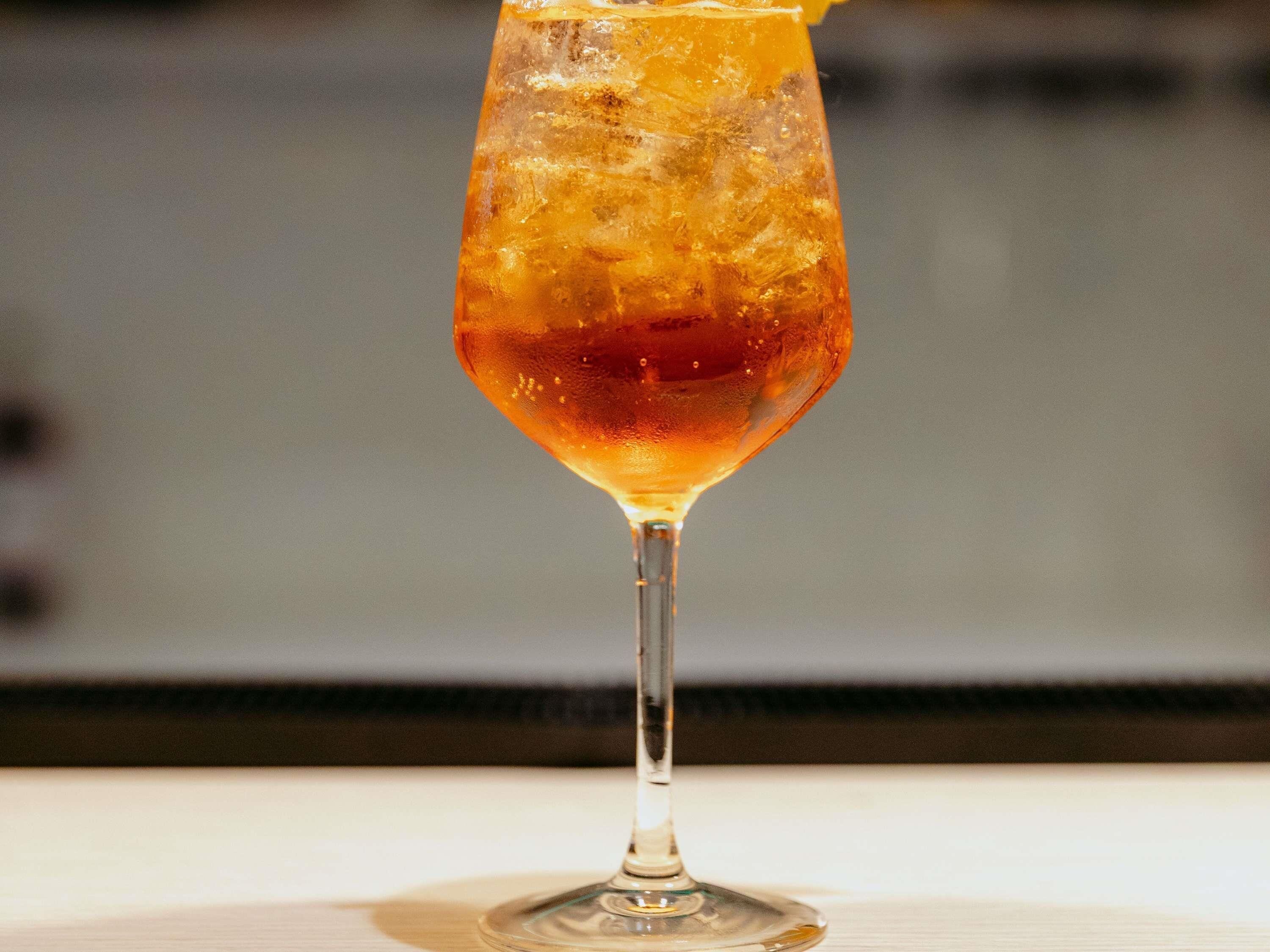 A tall glass with a clear stem, filled with a dark amber liquid and ice cubes.
