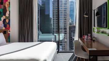 Una habitación de hotel con cama, escritorio, silla, televisor y vista a edificios altos.