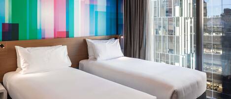 A hotel room with two beds, a colorful wall, a large window with a city view, and a modern design.