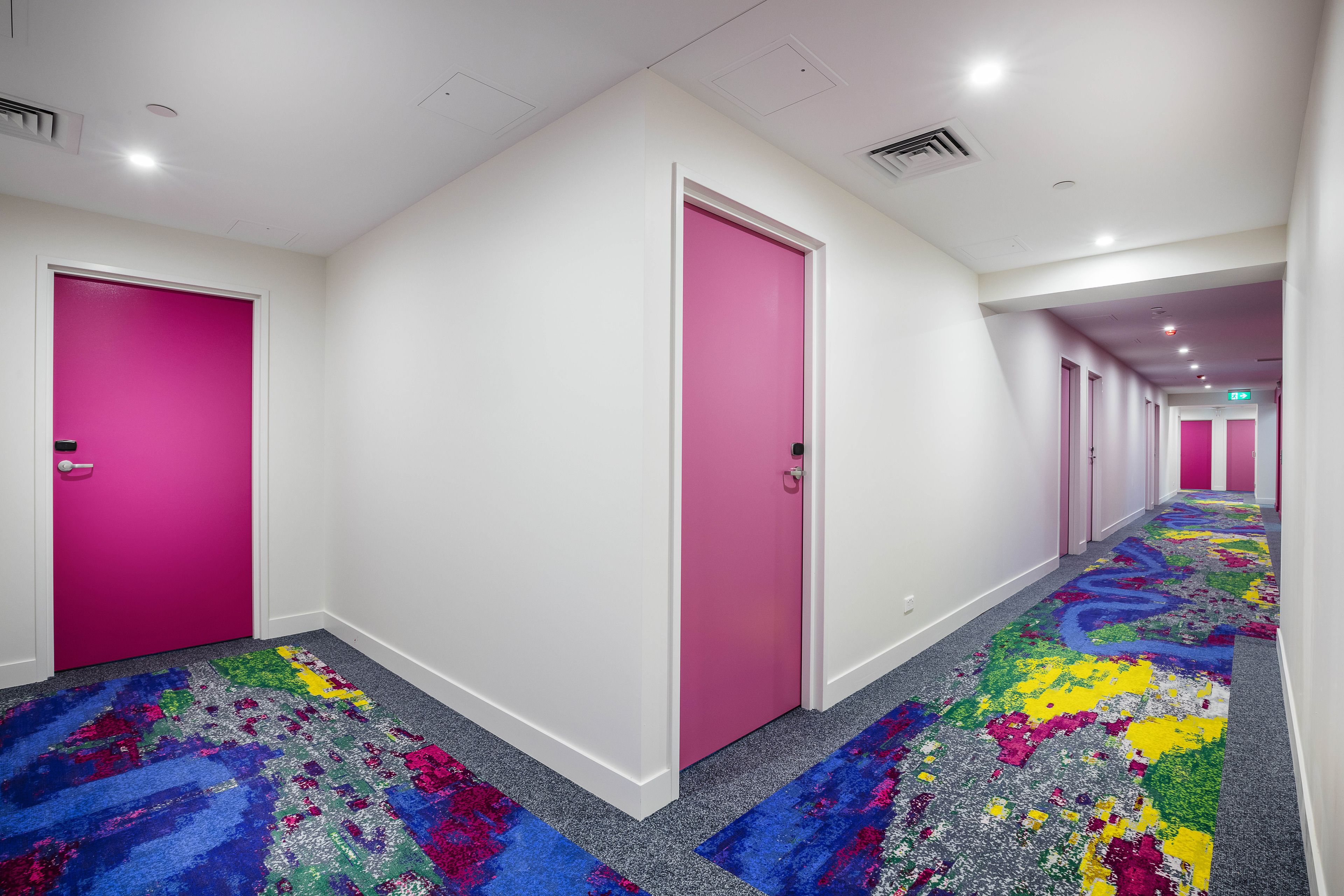 A hallway with pink doors and a colorful carpet.