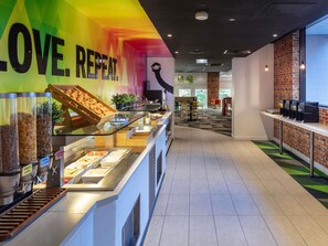 A breakfast buffet with various food options, a colorful wall with the text 'LOVE. REPEAT.', and a brick wall on one side.