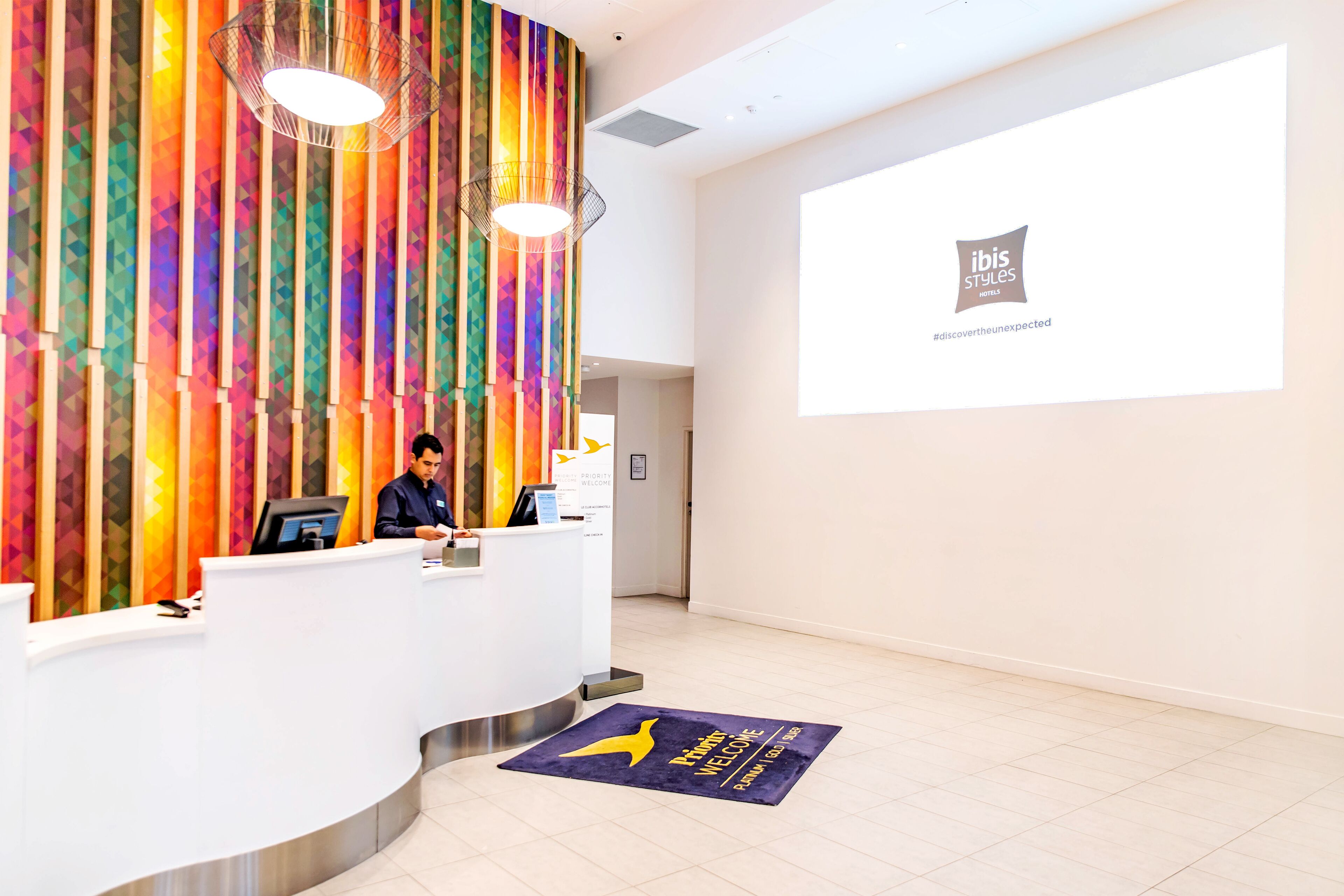A hotel reception area with a colorful vertical panel design, a reception desk, and a large screen displaying the hotel's logo.