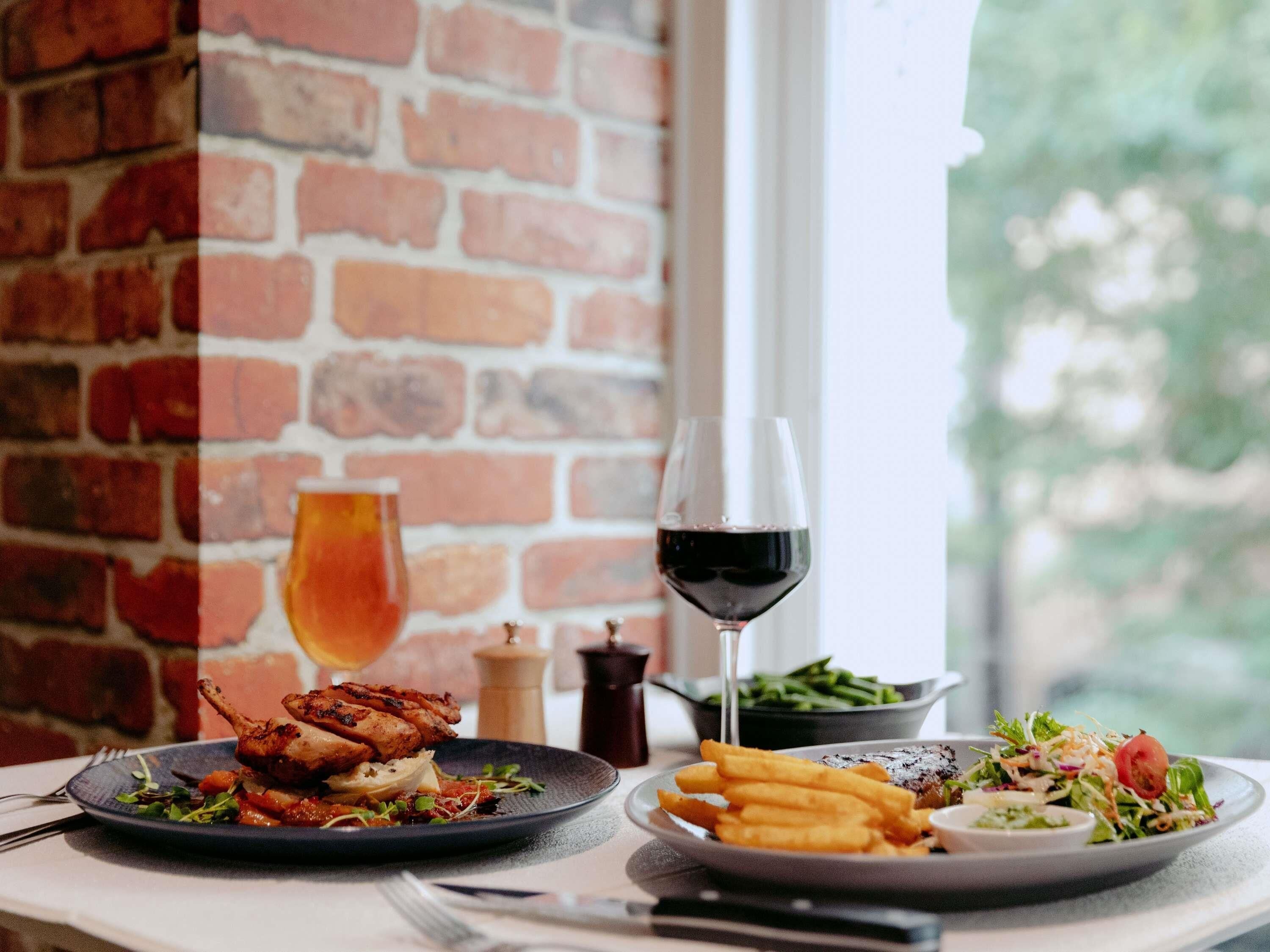 Een tafel met borden eten, een glas rode wijn en een bakstenen muur op de achtergrond.