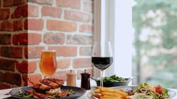 A table with plates of food, a glass of red wine, and a brick wall in the background.