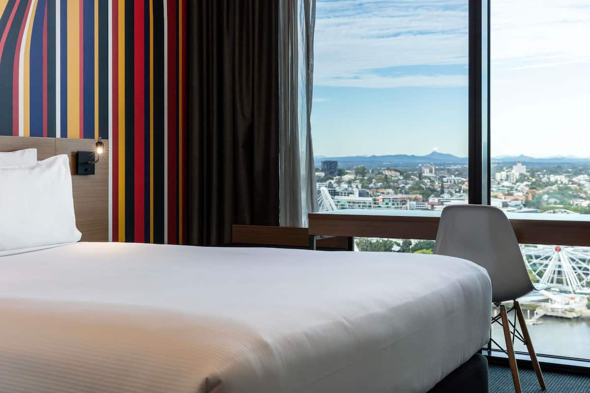 Une chambre d’hôtel avec un lit, une chaise, une vue sur la ville et une grande roue.