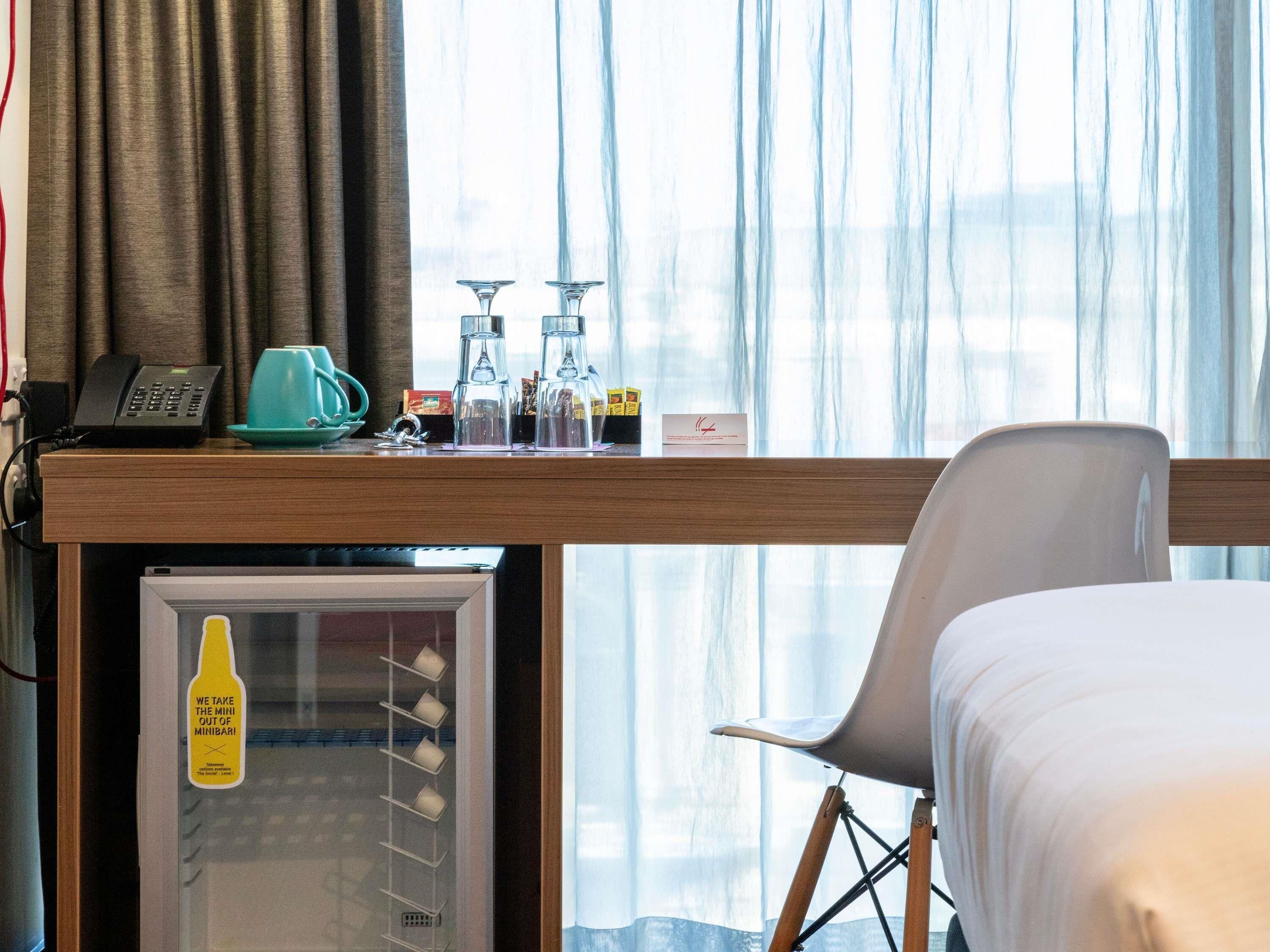 A hotel room with a bed, a desk with a phone, a coffee maker, and a mini fridge.