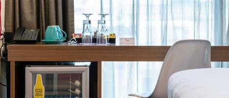 A hotel room with a bed, a desk with a phone, a coffee maker, and a mini fridge.