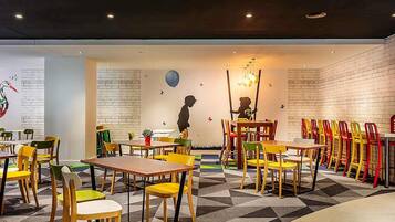 Un restaurante bien iluminado con sillas y mesas de colores, la silueta de un niño en la pared y un suelo con estampado geométrico.