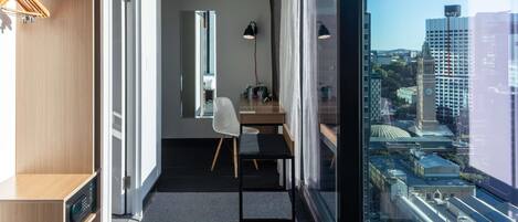 Habitación de hotel moderna con vista a la ciudad, un escritorio con silla, armario y un ventanal grande.