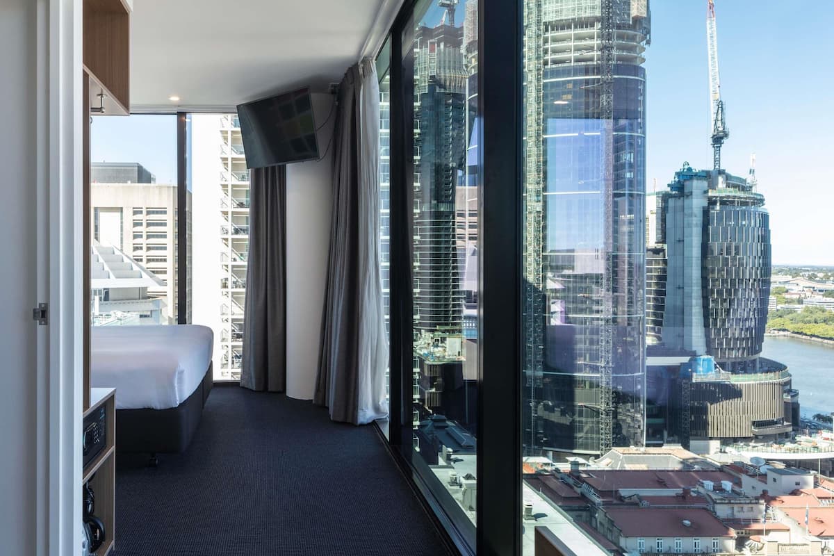 Une chambre d’hôtel avec un lit, une télévision, une vue sur la ville et une grande fenêtre.