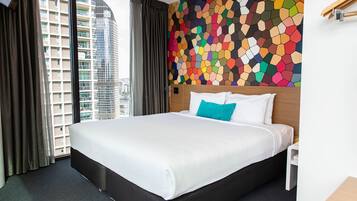 A hotel room with a large bed, a colorful mosaic wall, and a view of tall buildings through the window.