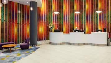 Un área de recepción con un muro geométrico y colorido, un mostrador de recepción y una zona de estar con un tapete estampado.