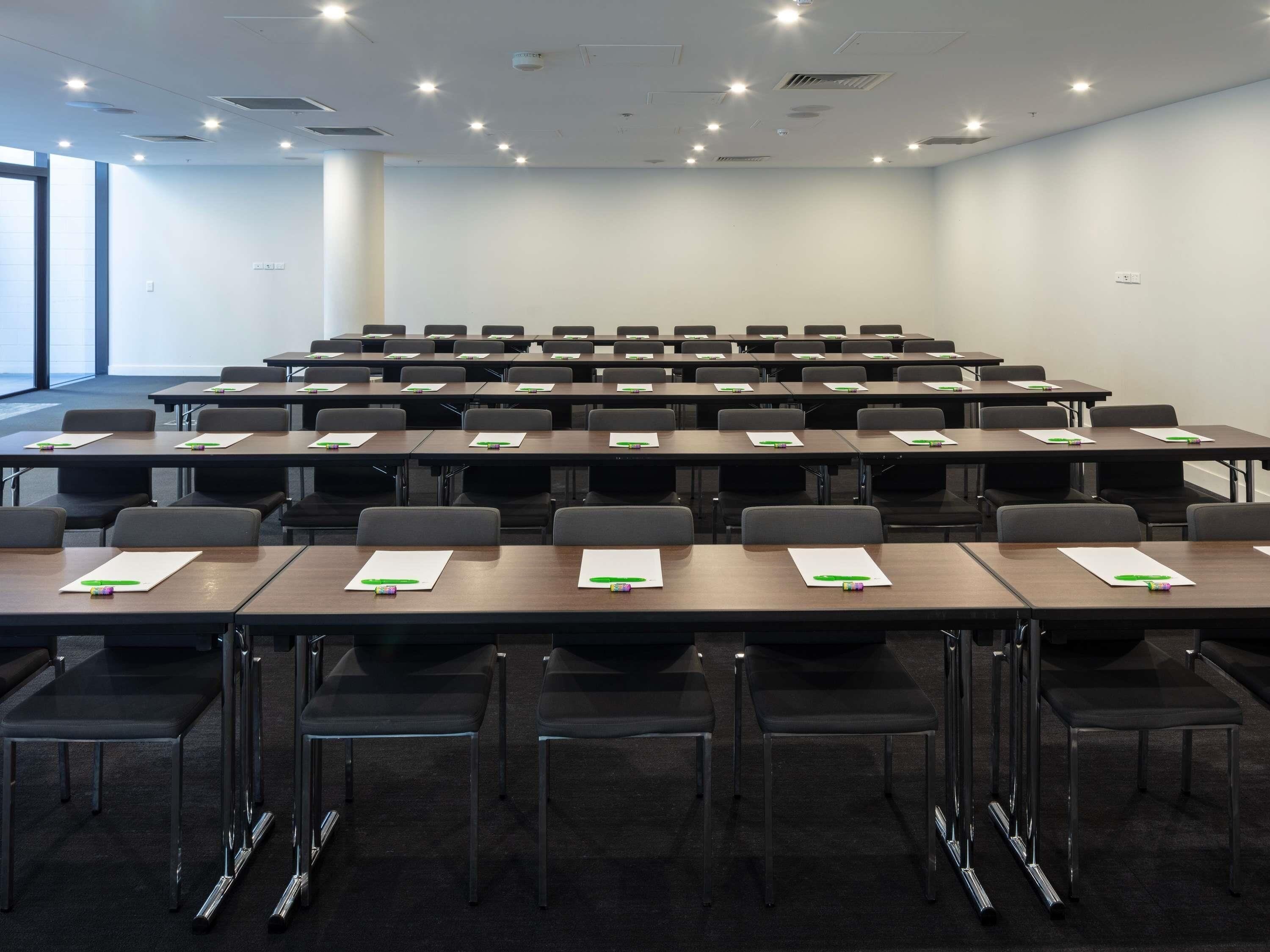 Un salón de conferencias con filas de mesas y sillas, equipado con tarjetas de identificación y bolígrafos.