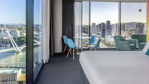 Habitación de hotel con una cama grande, dos sillones, una mesita y vistas a la ciudad y un puente.