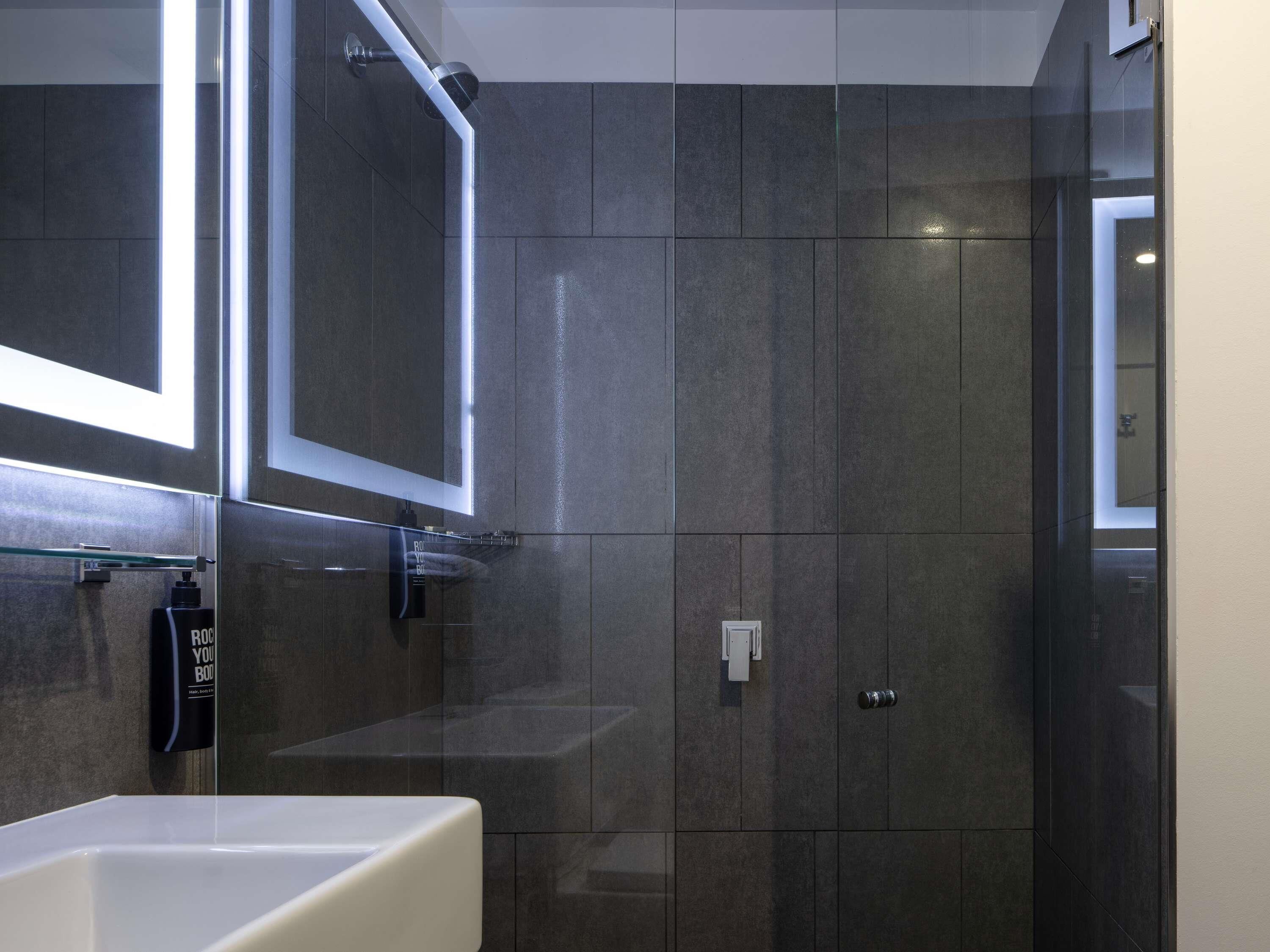 A modern bathroom with a large mirror, a glass shower enclosure, and a white sink.