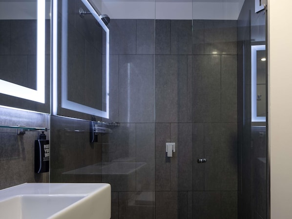 Une salle de bain moderne avec un grand miroir, une douche en verre et un lavabo blanc.
