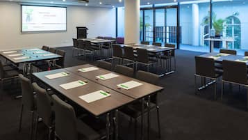 A conference room with tables, chairs, a projector, and a screen displaying 'welcome' in multiple languages.