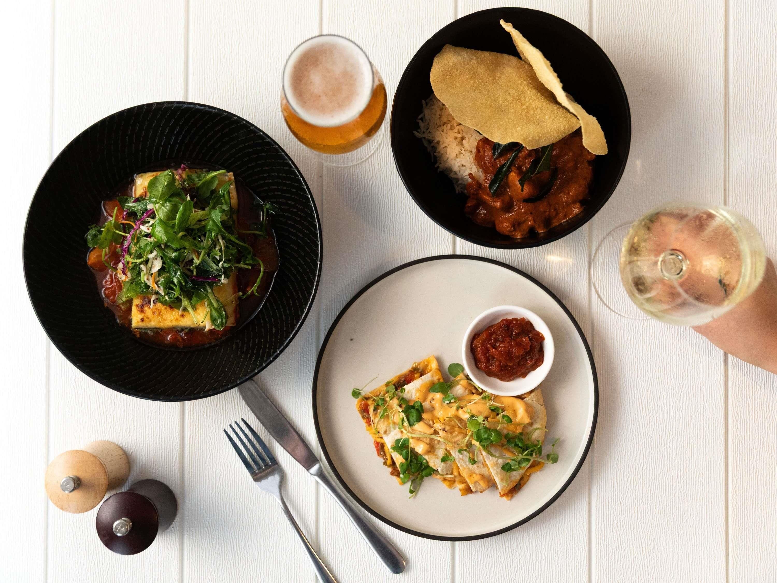 A table with three dishes, a glass of beer, and a glass of white wine.