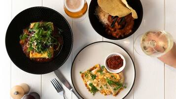 A table with three dishes, a glass of beer, and a glass of white wine.