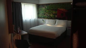 A hotel room with a bed, a desk, a chair, a nightstand, and a wall with a vineyard mural.