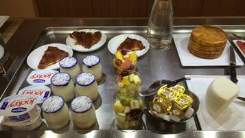 Un plateau contenant divers aliments, notamment du yaourt, une salade de fruits et un gâteau.