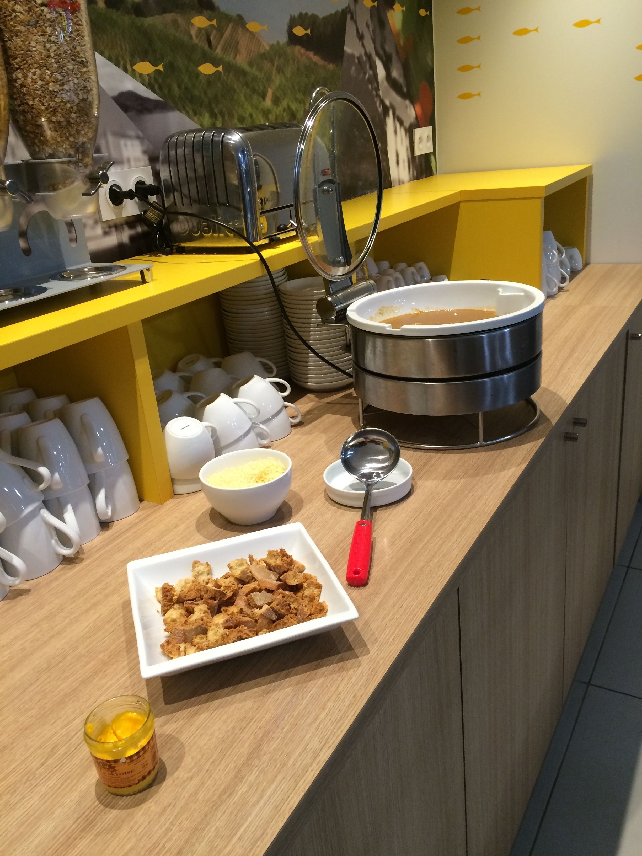 A breakfast buffet setup with a variety of food items, a coffee station, and a decorative wall.