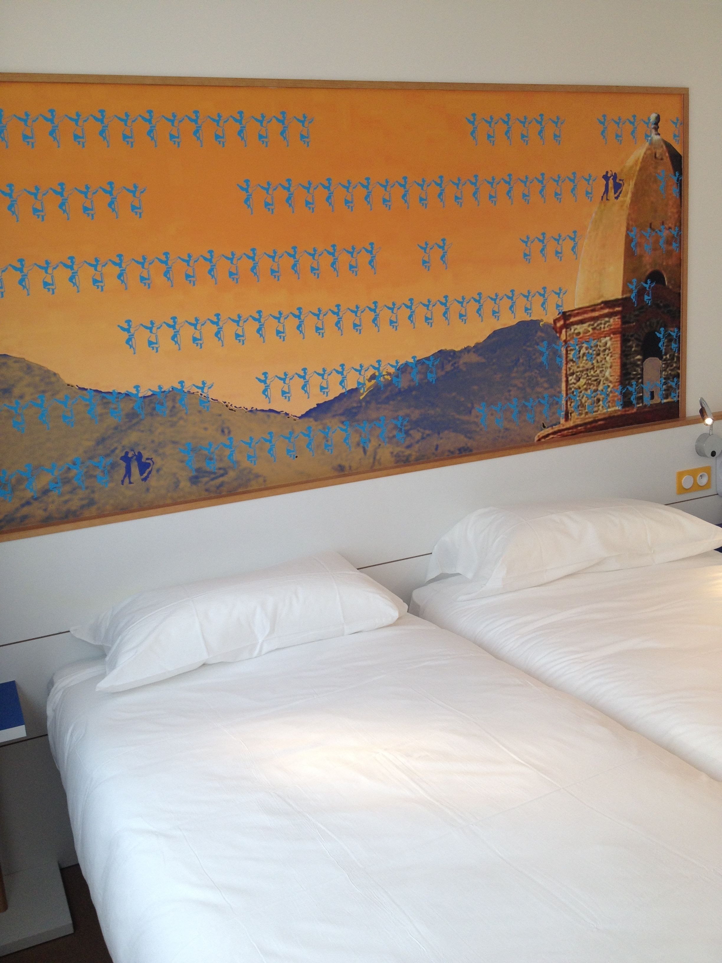 Una camera d'albergo con due letti, un quadro grande appeso al muro e un comodino con una lampada.