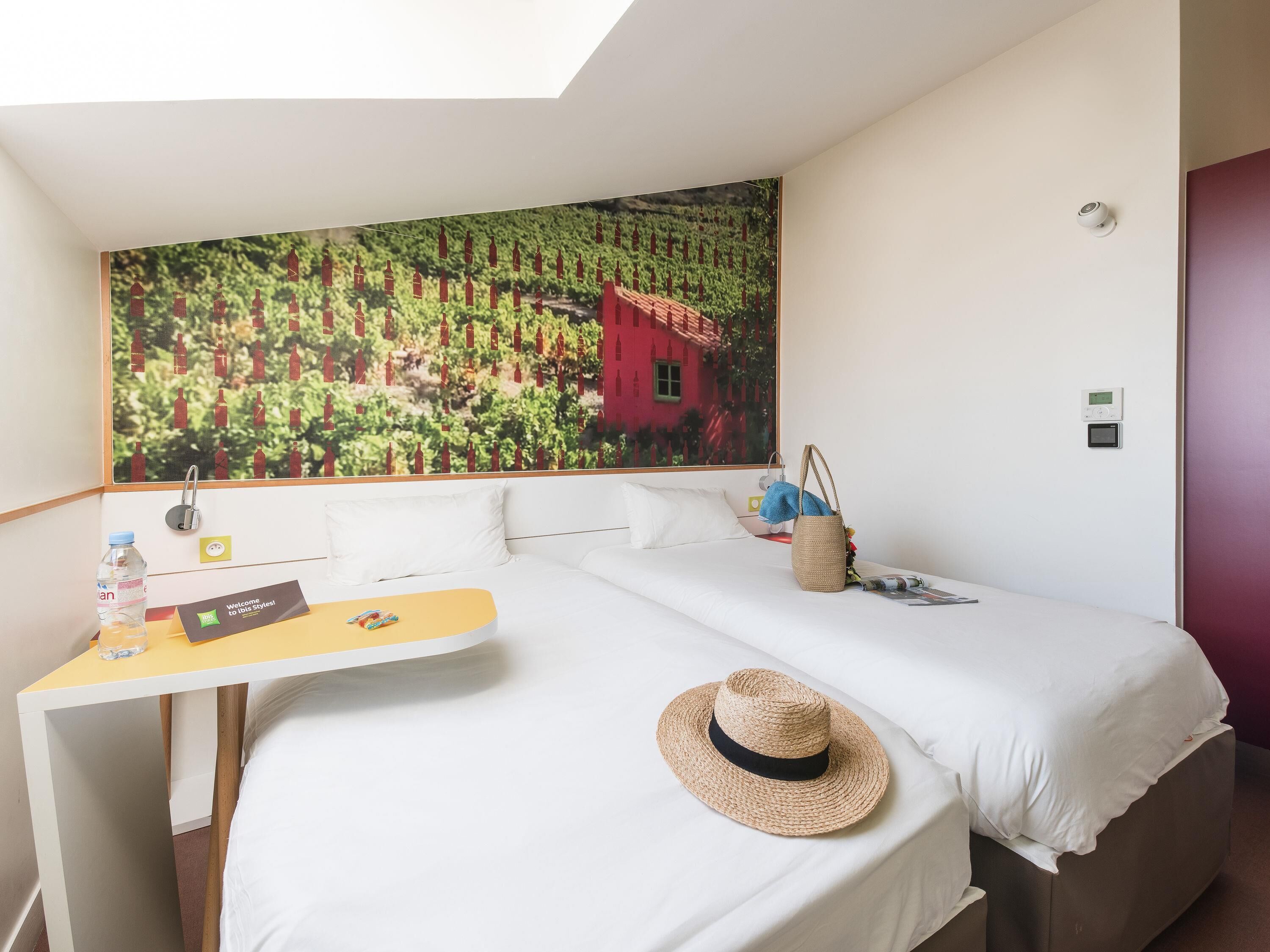 Habitación de hotel con cama, un pequeño escritorio, aire acondicionado de pared y un cuadro de un viñedo.