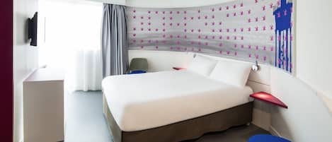A modern hotel room with a curved bed, a desk, a chair, and a large window with curtains.