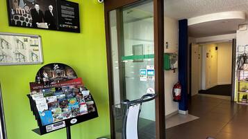 A hotel lobby with a green wall, a glass door entrance, a display rack with brochures, and a fire extinguisher.