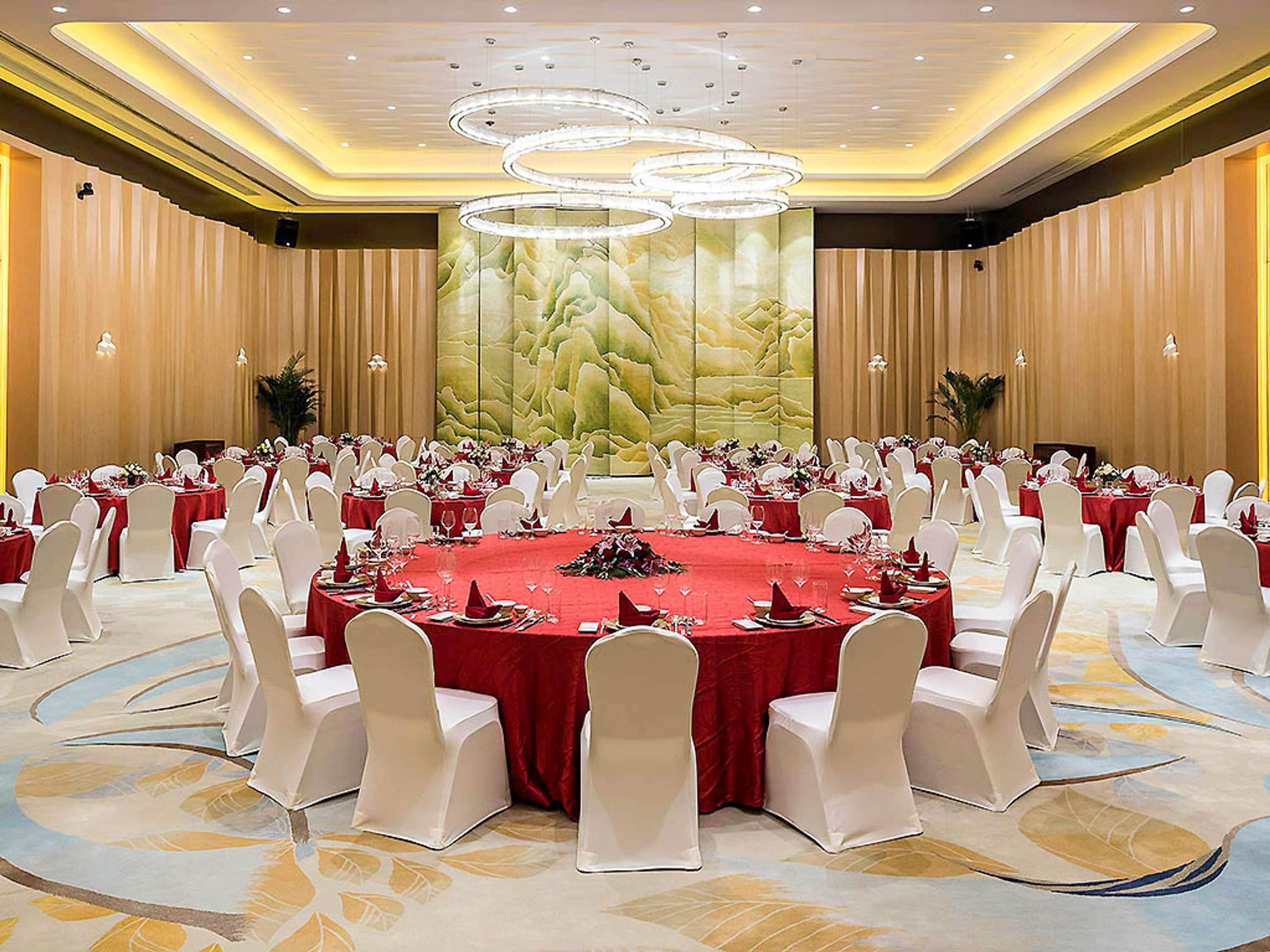 A large conference room with round tables, white chairs, and red tablecloths.